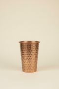 A hammered copper-colored decorative vase featured in a light ivory study background. 