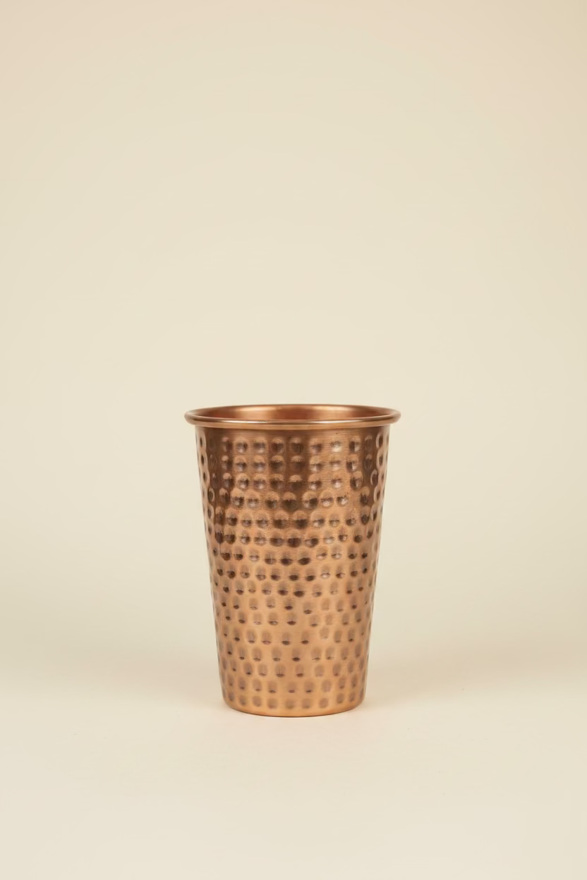A hammered copper-colored decorative vase featured in a light ivory study background. 