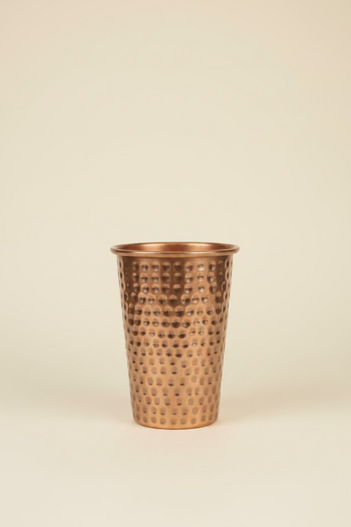 A hammered copper-colored decorative vase featured in a light ivory study background. 