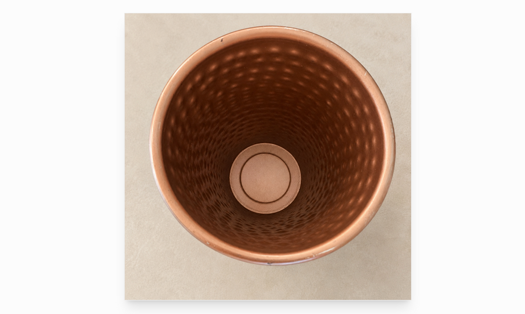 Photo of the inside of a copper-toned metal vase on an ivory background. 