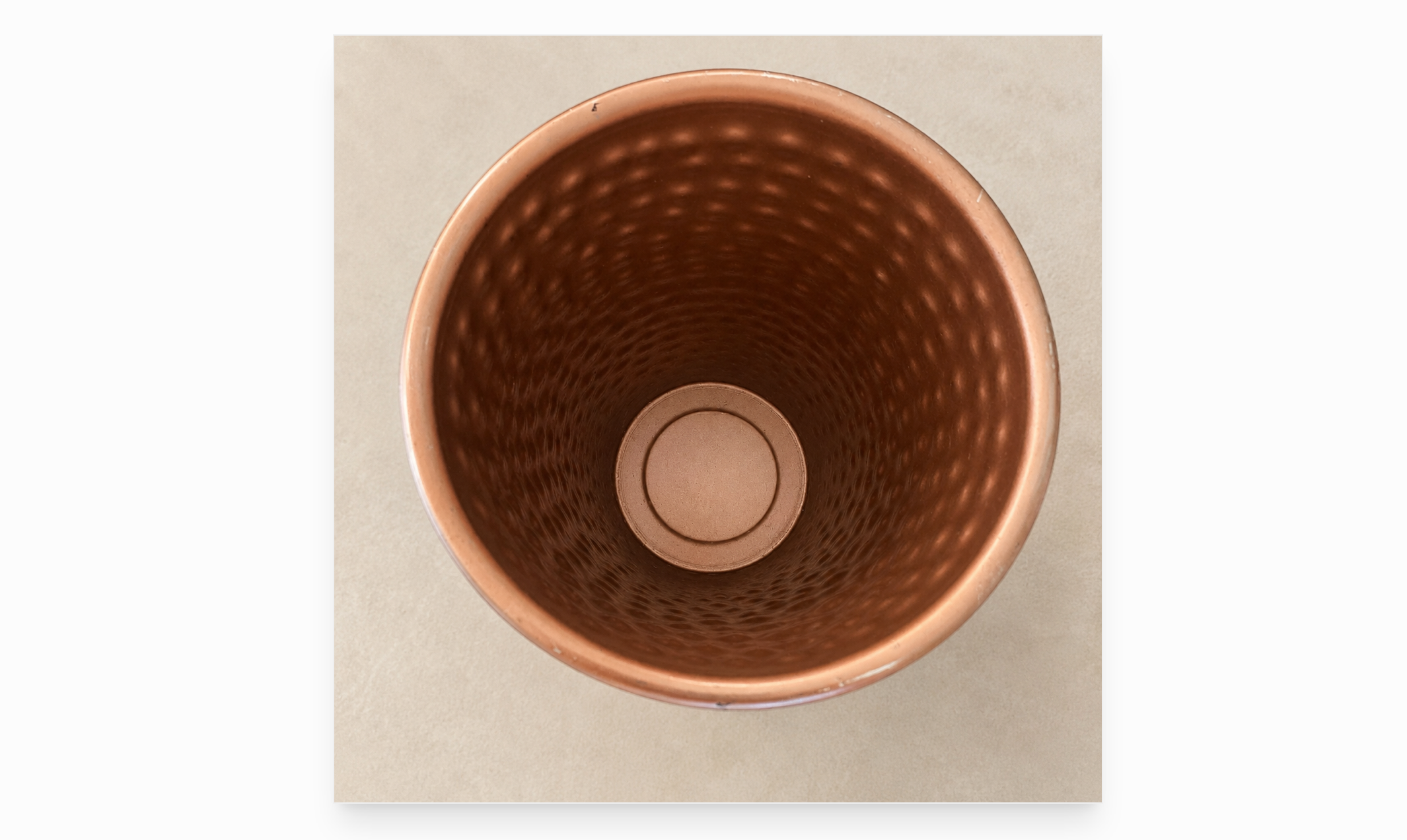 Photo of the inside of a copper-toned metal vase on an ivory background. 