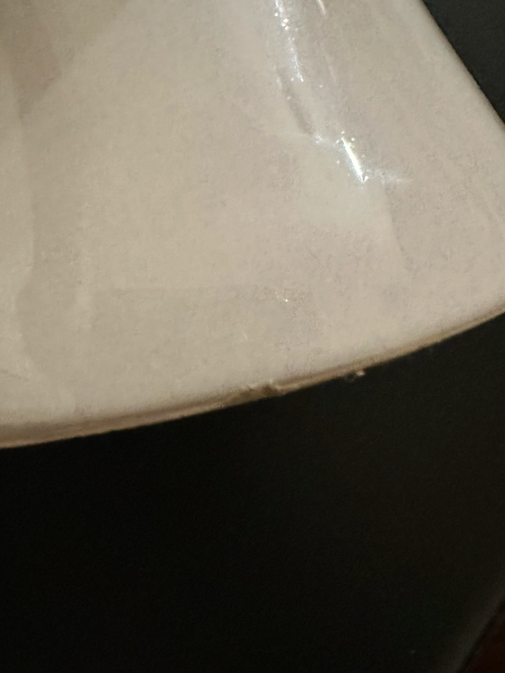 A close-up of a glossy off-white ceramic surface, with a dark black background showing a small chip near the base of the vase. 